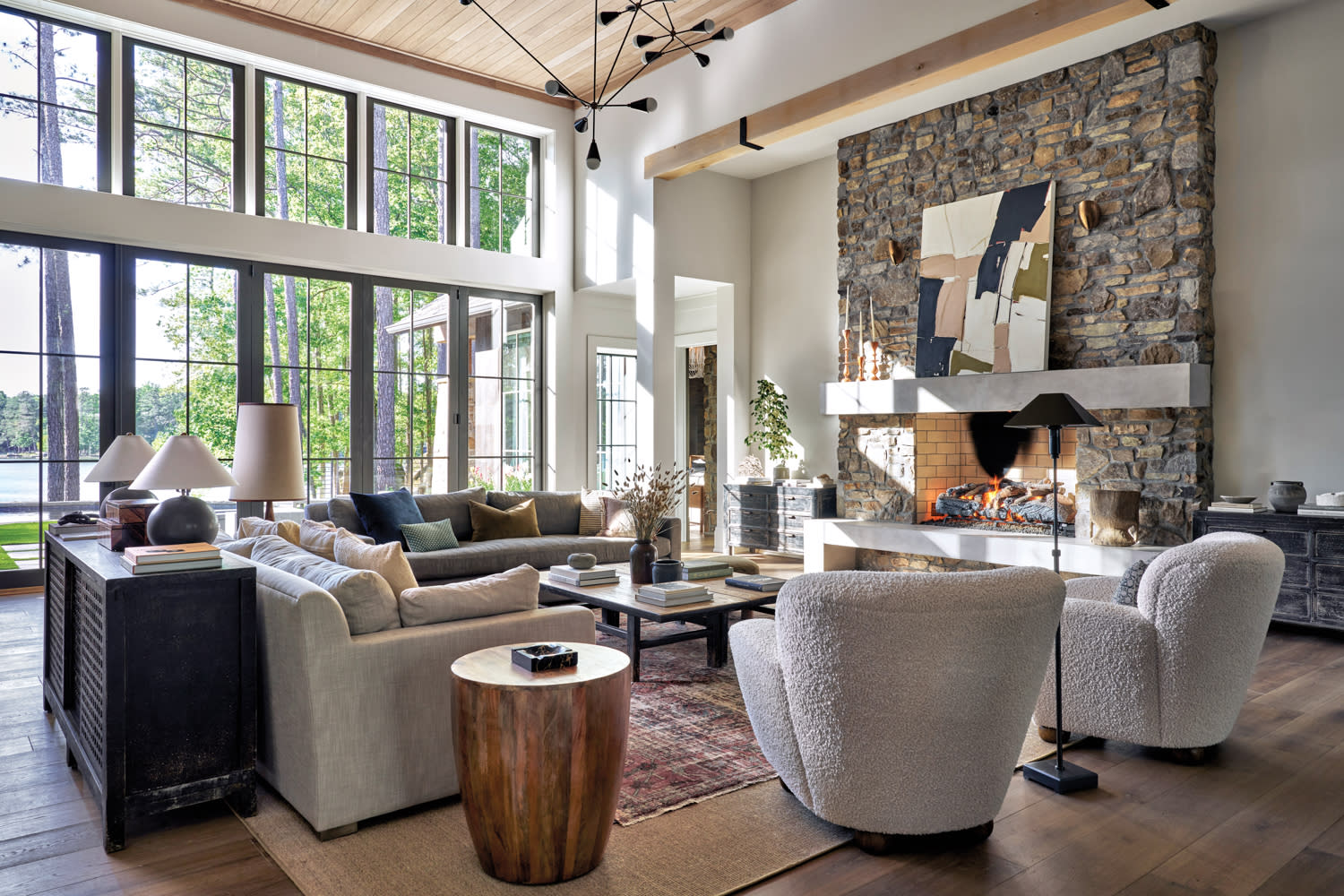 Sunlit living room with tumbled stone fireplace, modern chandelier and light-colored upholstery