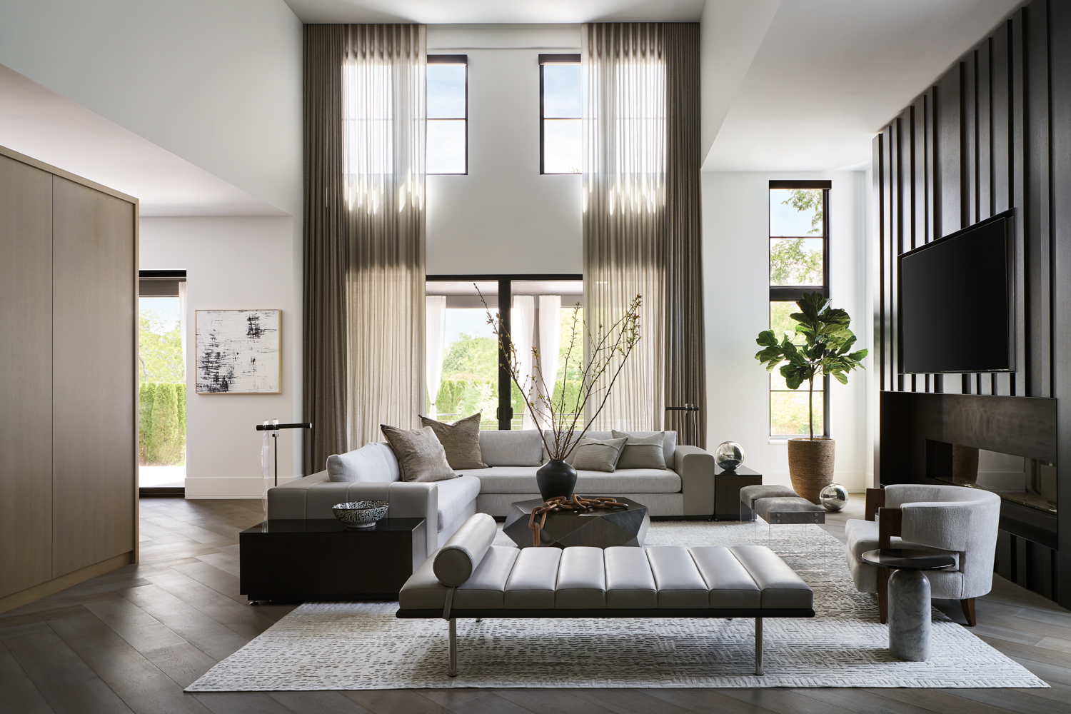 double-height living room with leather-and-boucle gray sectional, gray faux leather chaise and a paneled fireplace