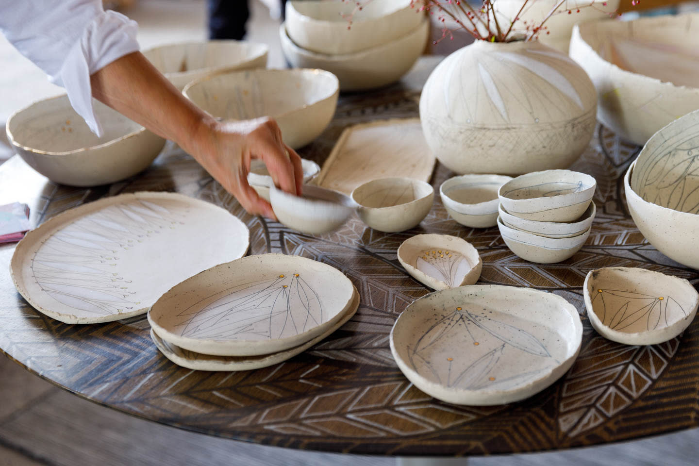 a person reaches for a white ceramic bowl in a display of assorted ceramic dishware