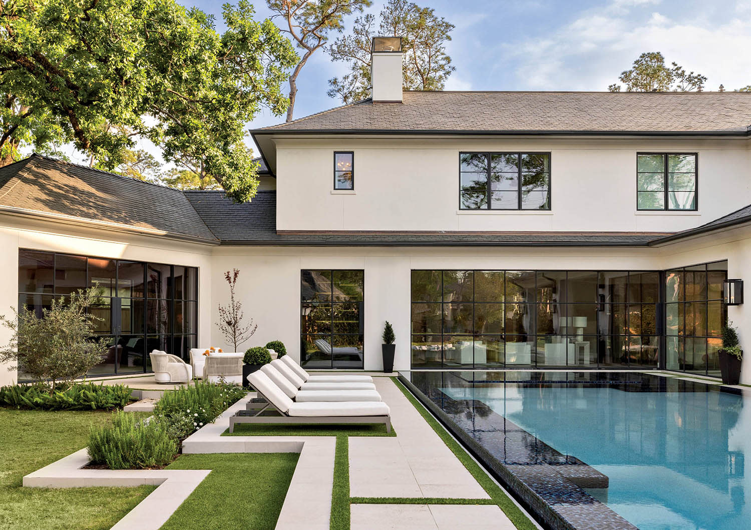 A backyard bordered by grass, a seating area, and a row of lounge chairs next to a swimming pool