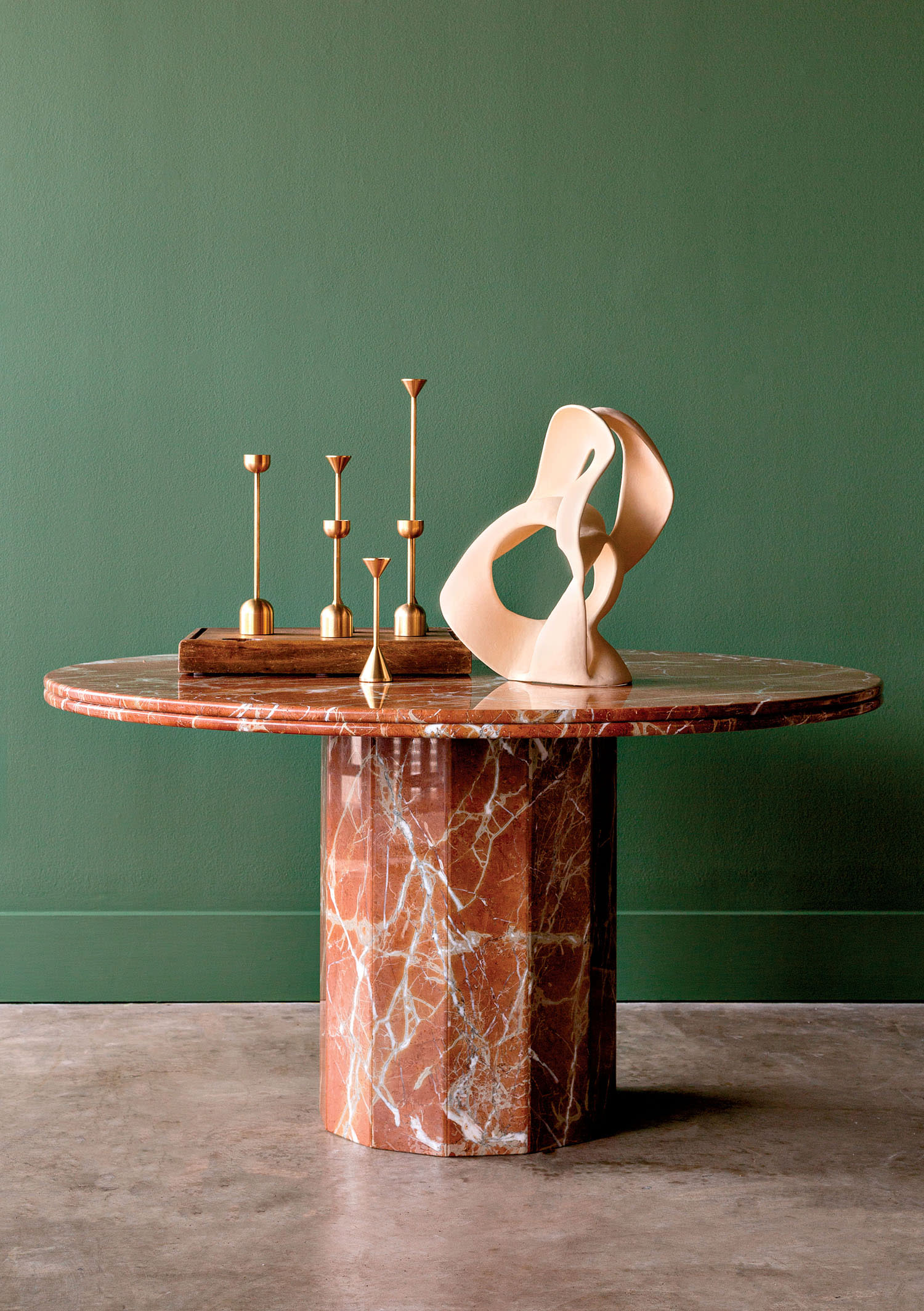 A round table with a sculpture on top sits in front of a bright green wall.