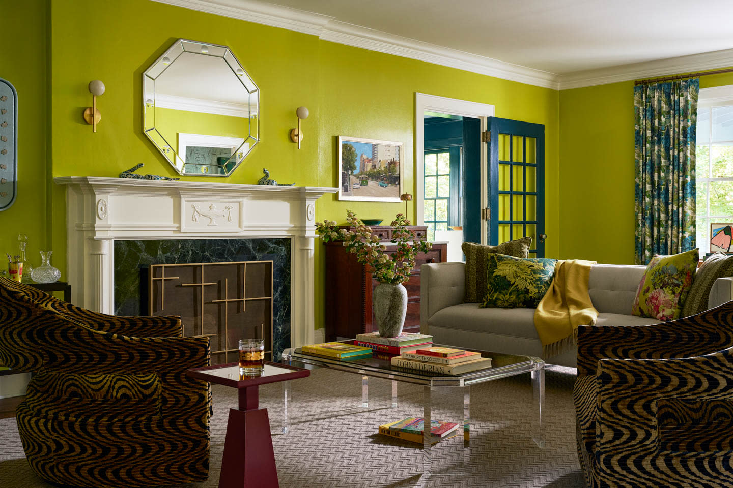 A vibrant living room with lime green walls, ornate fireplace, and eclectic decor. The room features a gray sofa, patterned chairs, and colorful accents, creating a lively yet cozy atmosphere.