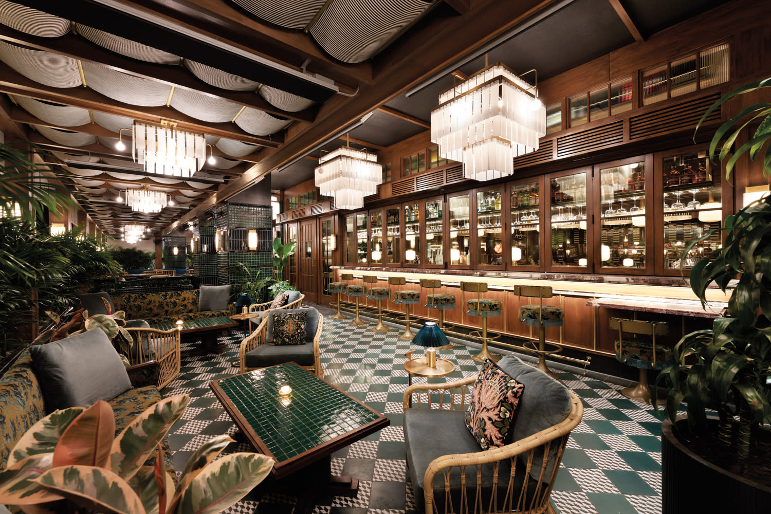 Restaurant bar area with wood walls, green checkered tile floors, woven seating and geometric chandeliers.