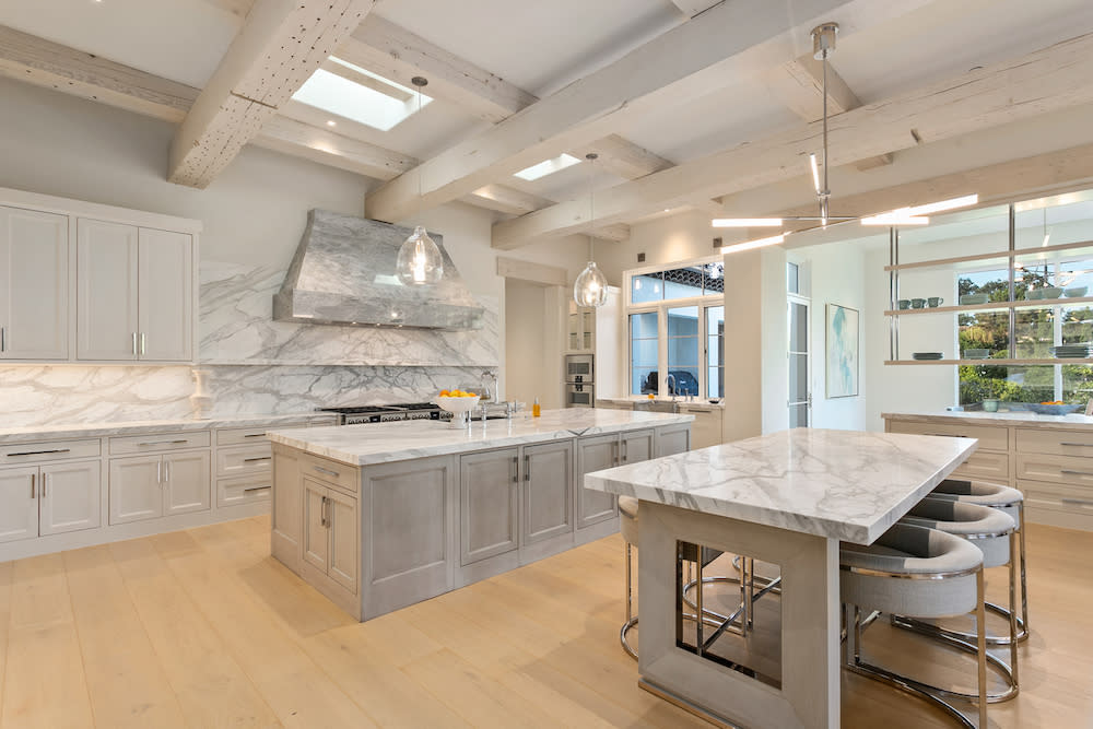 White and grey kitchen with marble island and large center island, featuring modern appliances and ample seating.