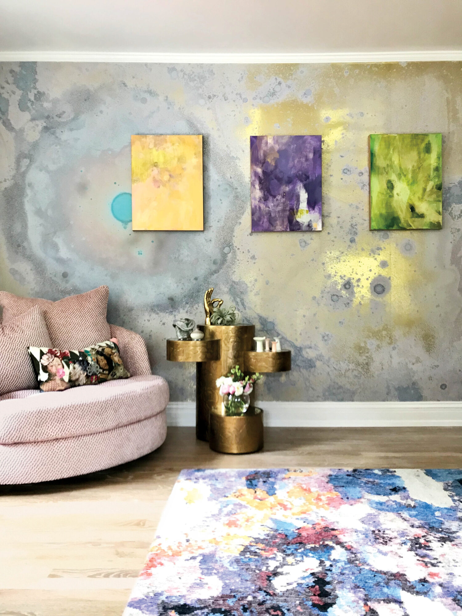 vignette of pink chair, colorful rug and yellow, purple and green artworks