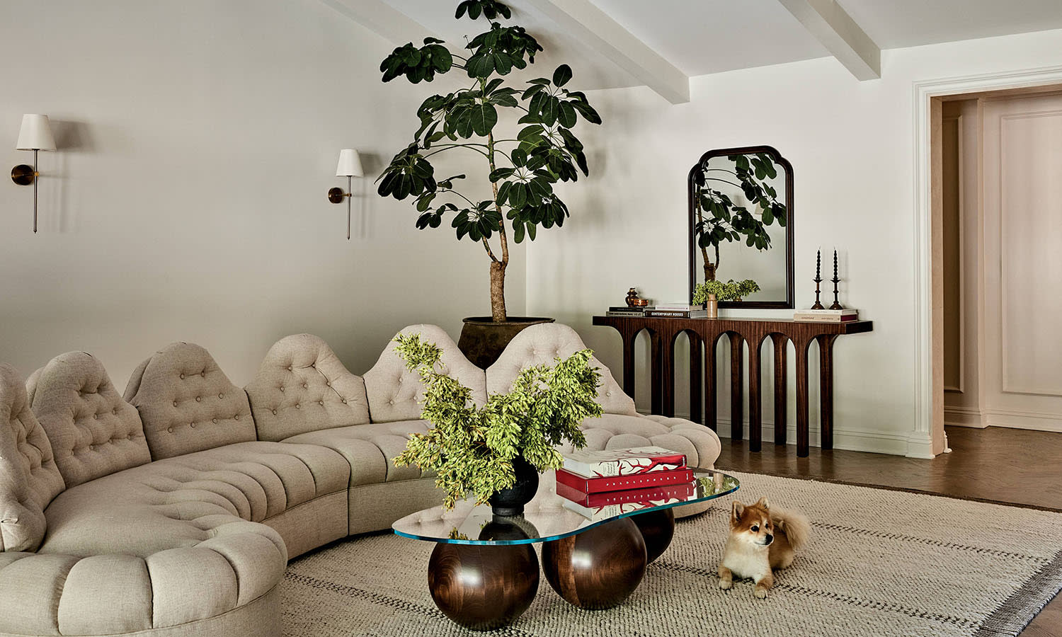 A curved white couch sits on a white rug with a small dog lying down next to a coffee table.