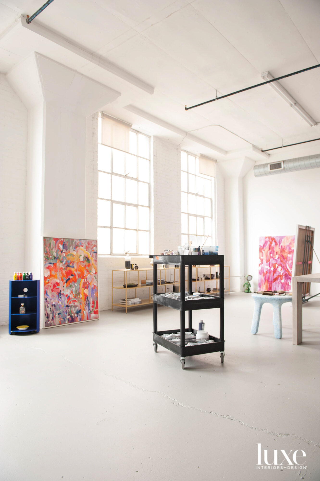 A large white studio with large windows and two colorful abstract paintings.