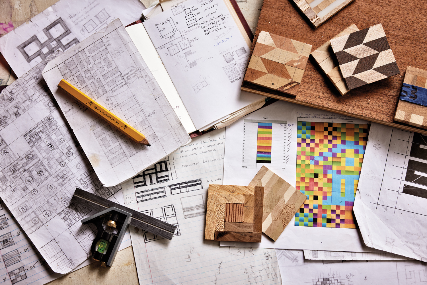 Tabletop scattered with notebooks, inspiration drawings, tools and small wooden mosaic tiles