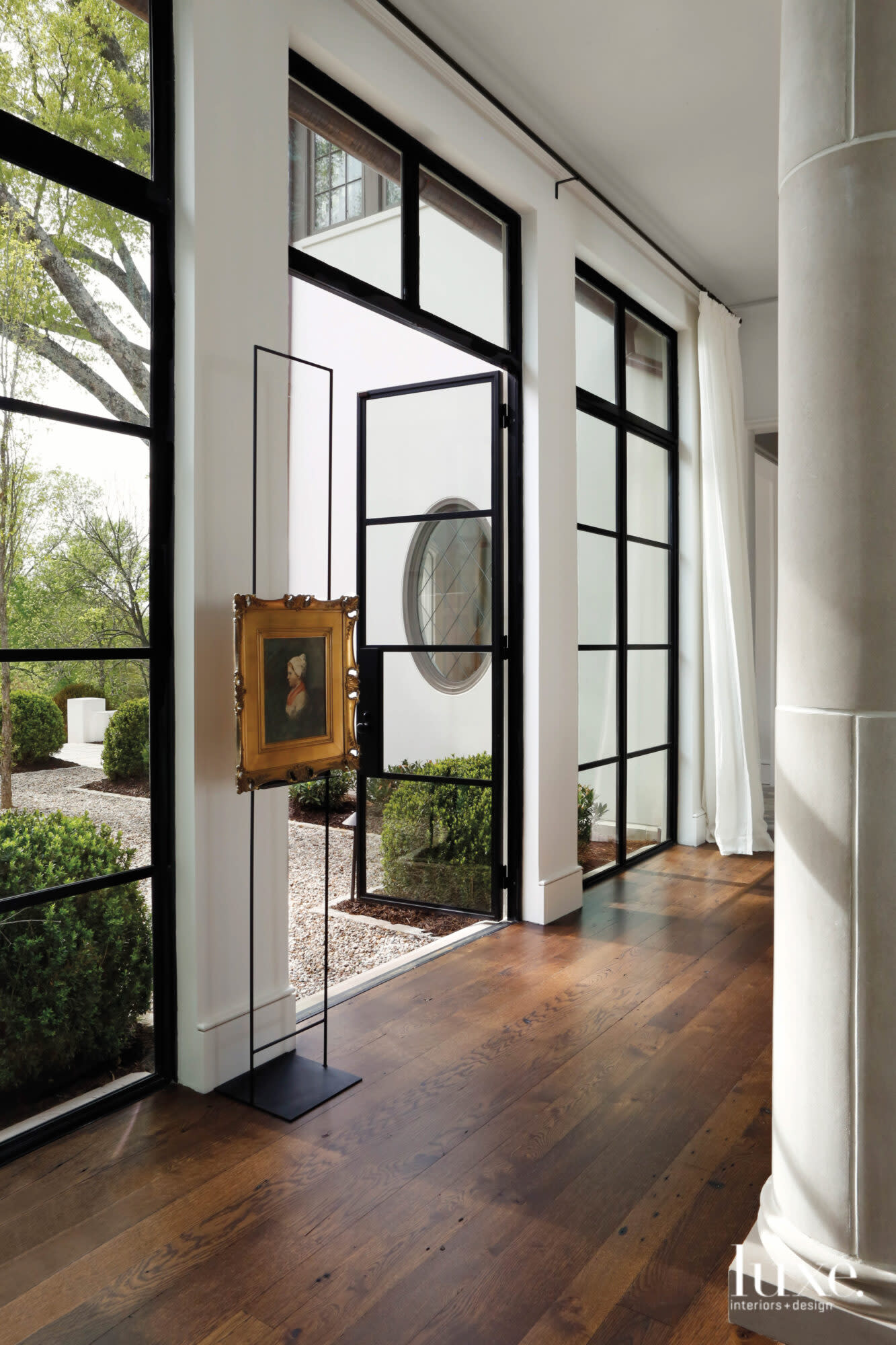 Dark wood floors and steel French doors lead to a breezy courtyard with pea gravel and clipped boxwoods