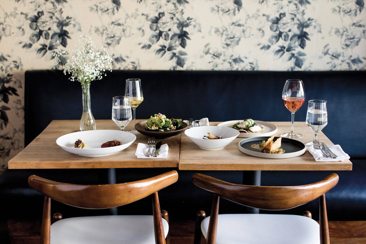 Restaurant with wood tables and blue banquettes set against blue-and-cream floral wallpaper