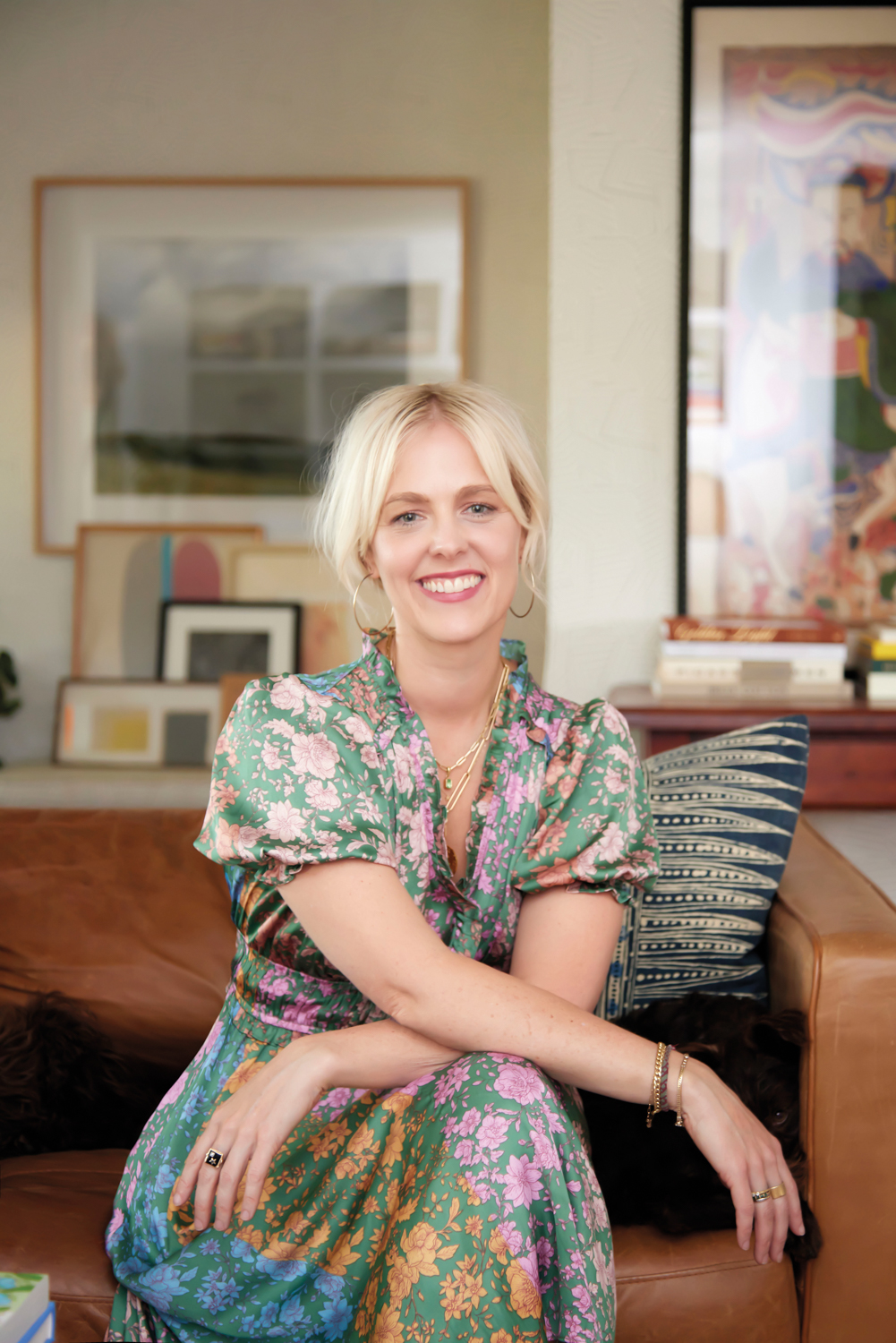 Meg Kelly sitting on a leather couch in a colorful floral dress.