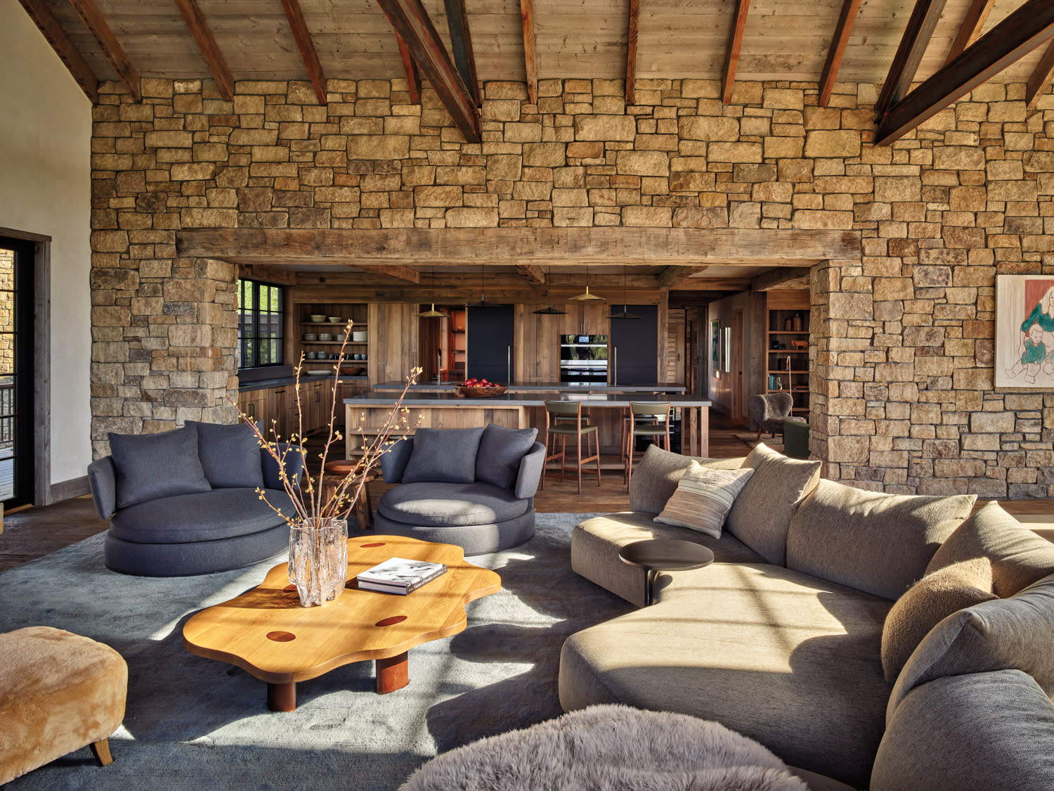 A cozy living room featuring a stone wall and a comfortable couch, creating a warm and inviting atmosphere, opens to a kitchen