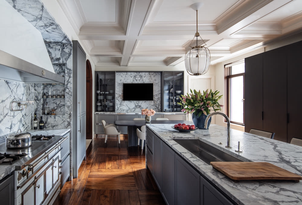 With the coffered ceiling, blue-gray cabinets, gray marble counters, and hardwood floors, the kitchen likely exudes a harmonious blend of modern and classic elements.