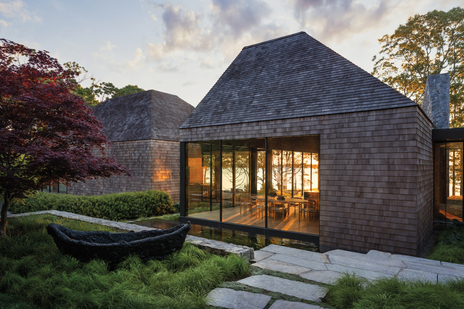 a cedar-clad home's dining room is seen from outside at dusk