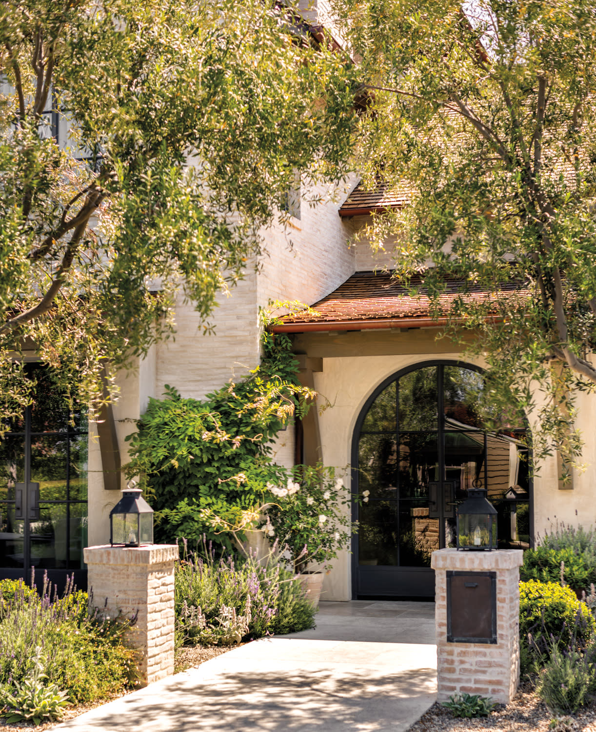 Brick exterior facade of a Mediterranean style home by Marie Carson with arched glass entry door and red terracotta tile roofing