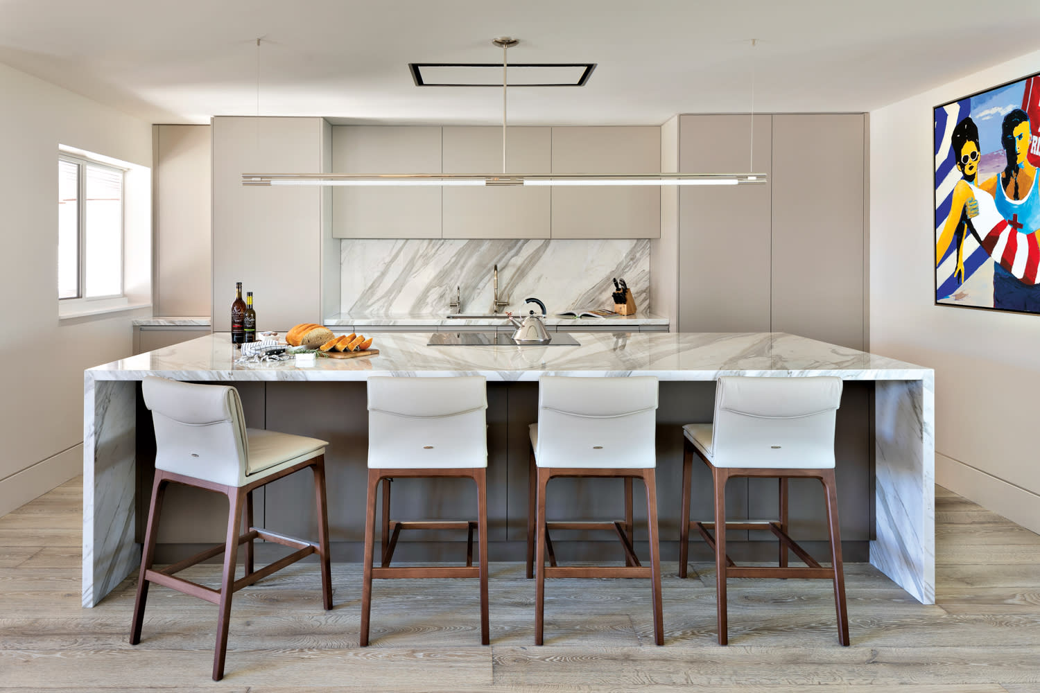 Sleek kitchen with white-marble waterfall island lined with highback chairs.