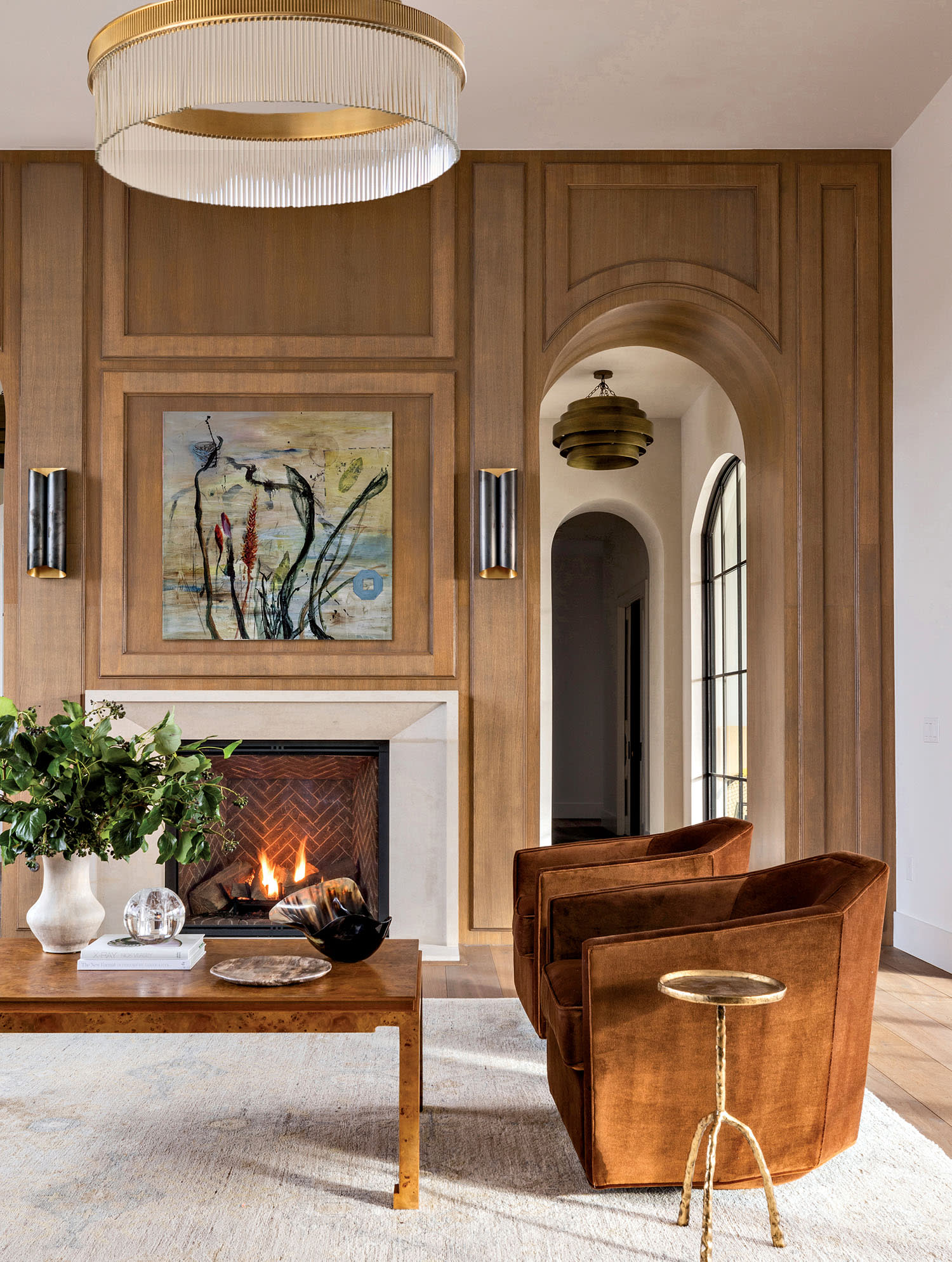 A living room with oak paneled walls, artwork above a fireplace and chairs set alongside a table.