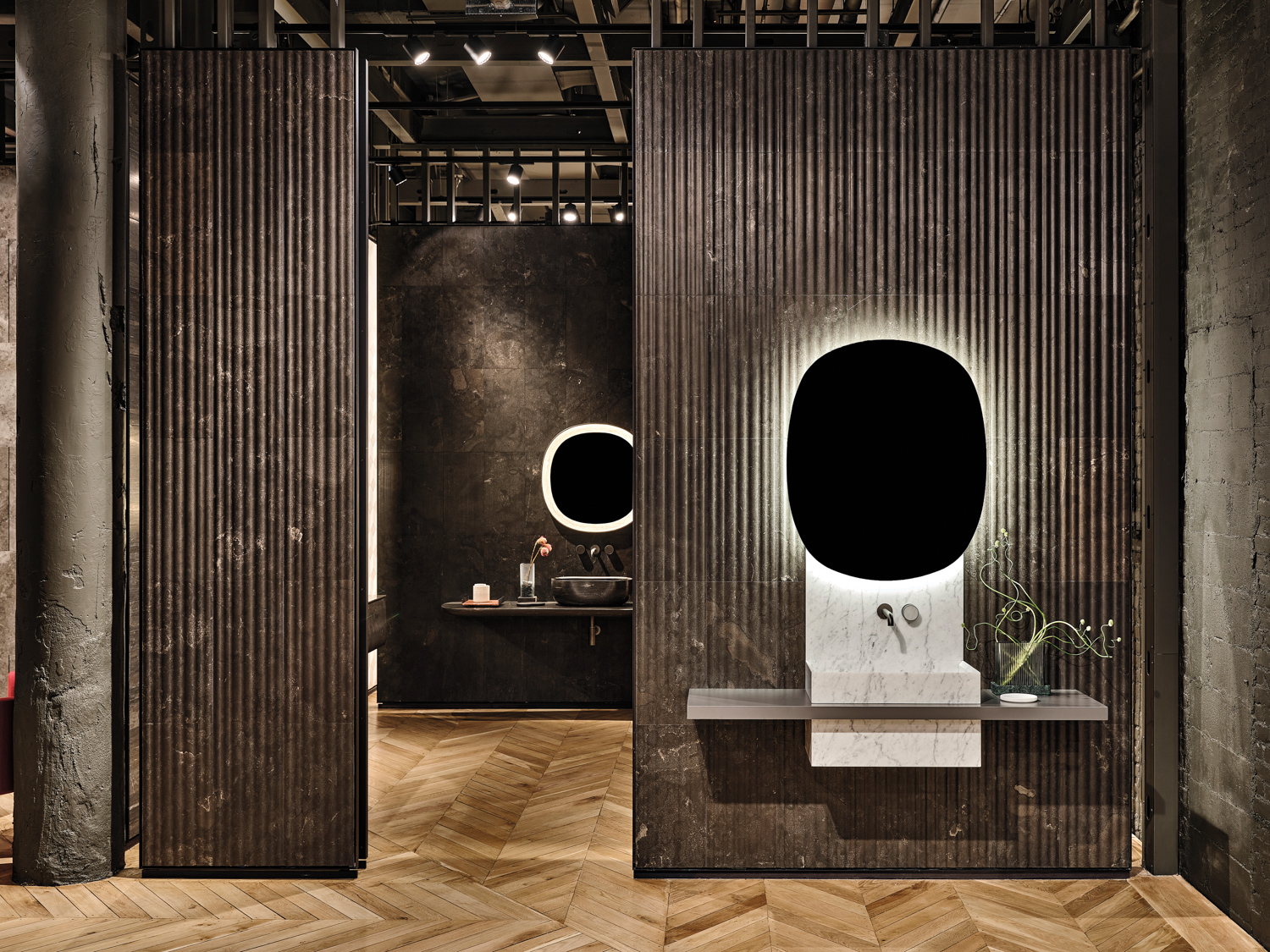 A vanity on display in a showroom with a backlit, oval mirror against a fluted dark wood wall