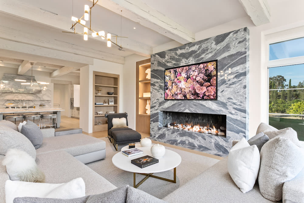 A spacious living room featuring marble fireplace, white furniture and a large TV.