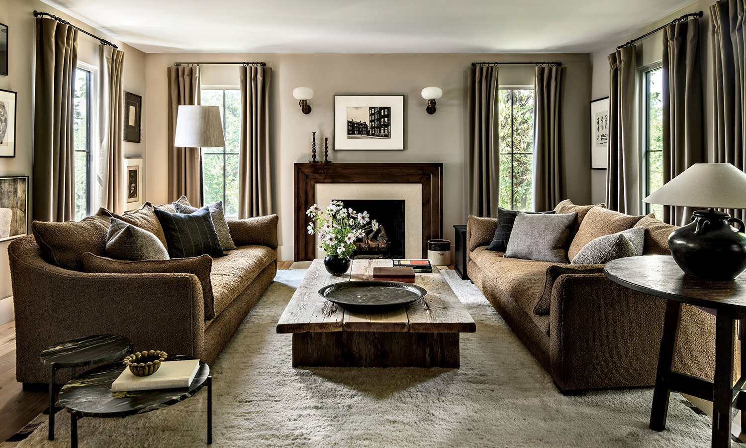 Cozy living room with two brown sofas facing each other, a rustic wooden coffee table, and a fireplace. Soft lighting and earth tones create a warm, inviting atmosphere.