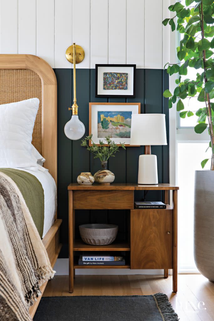 Clasen painted the lower half of a wall in the master bedroom Benjamin Moore's Wrought Iron. An Indian throw from Hollywood at Home covers the Lind + Almond bed. The nightstand, topped by a Stone and Sawyer lamp, is by Hedge House Furniture. The sconce is by Michele Varian.