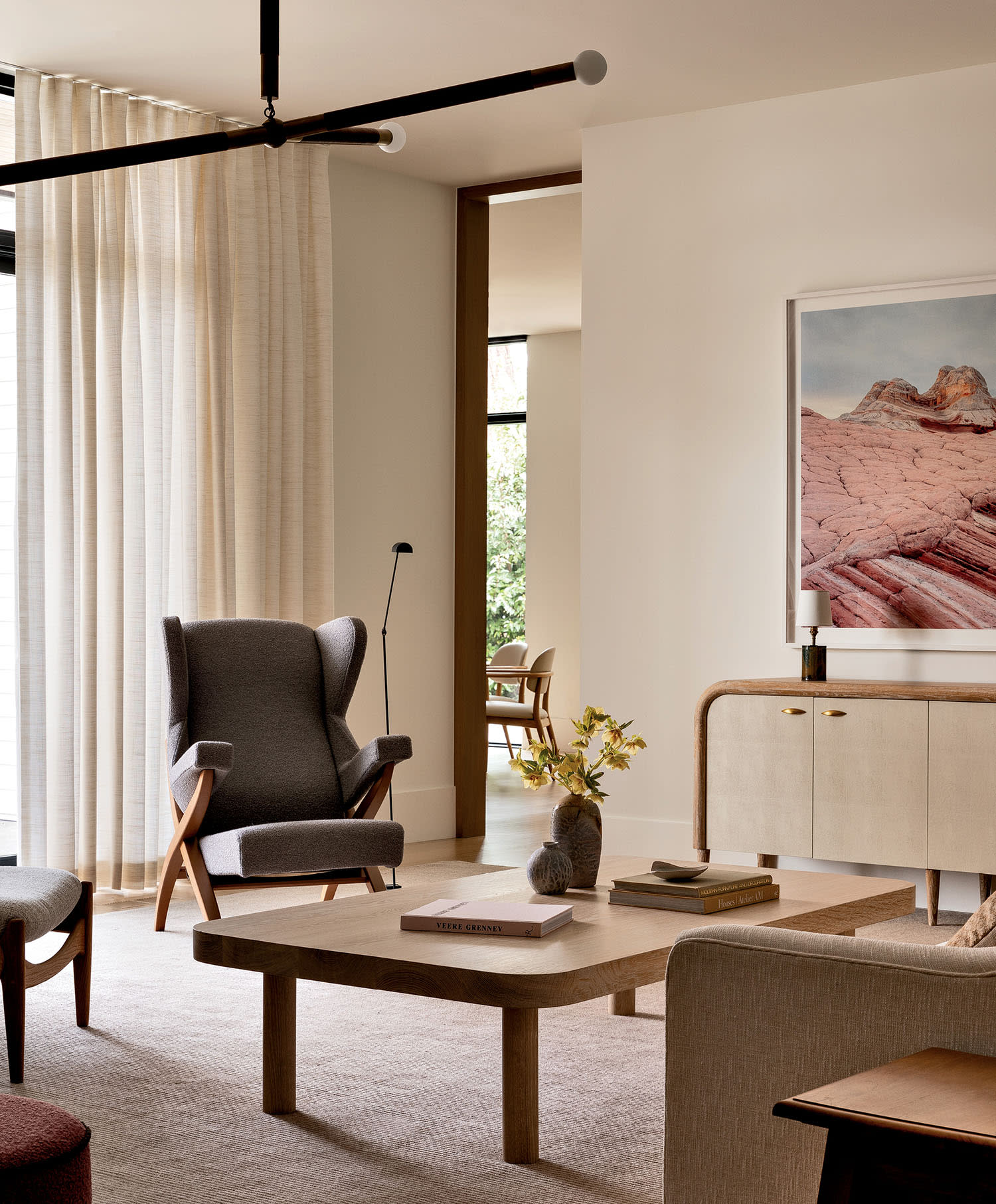 Modern living room with neutral tones, featuring a gray armchair, wooden coffee table, sideboard, abstract art, and soft lighting, creating a serene ambiance.