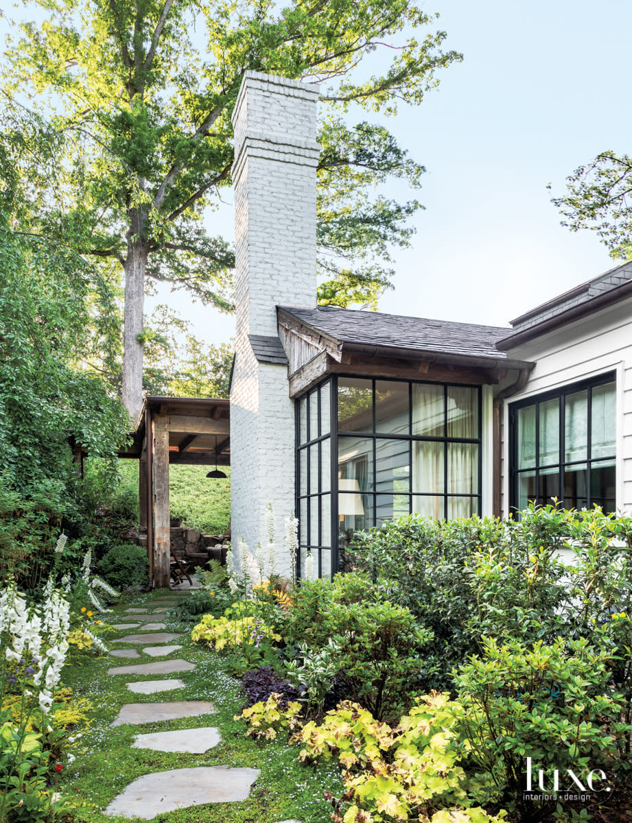 lush garden surrounding white brick house and sunroom