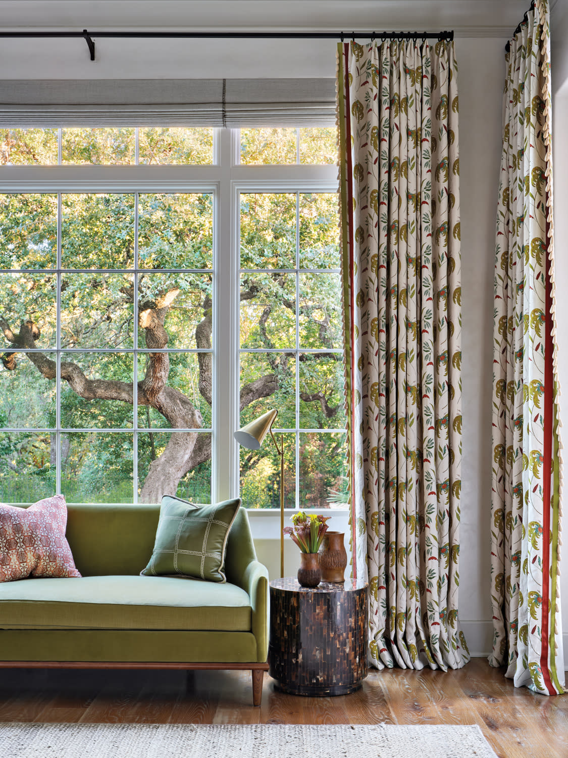 Bedroom with green sofa, colorful pillows and patterned drapes against a large window