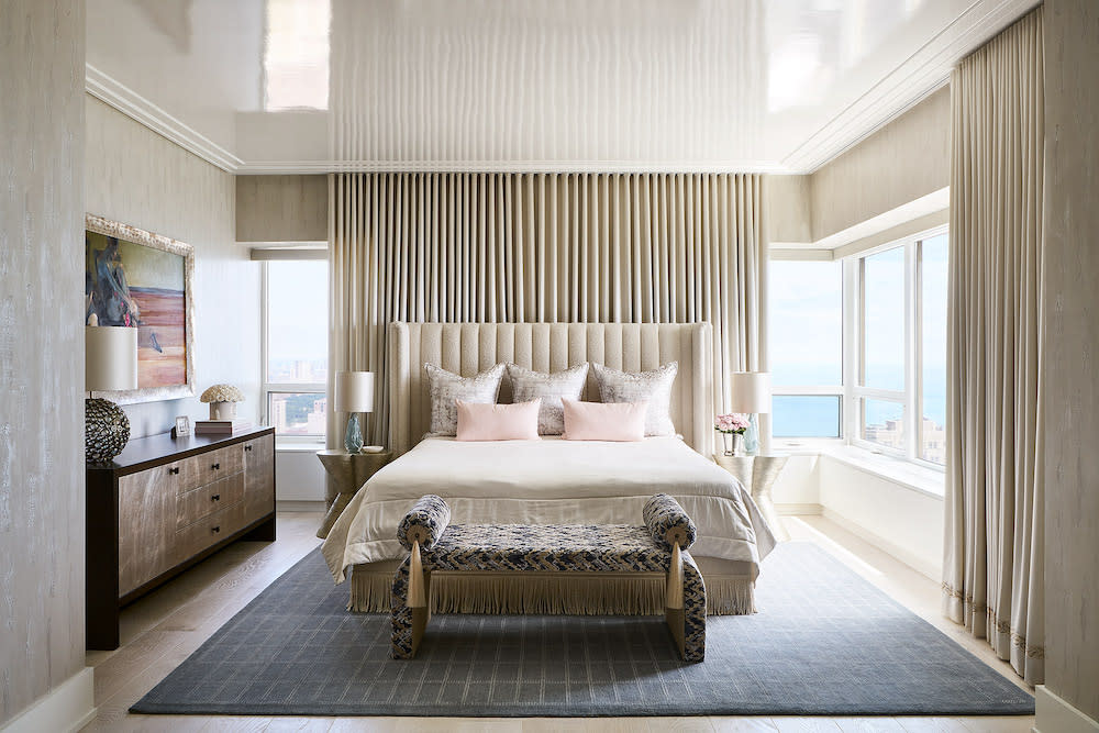 Beautiful views from the walls of windows in this serene primary bedroom. Cream upholstered headboard and high gloss paint on the ceiling.