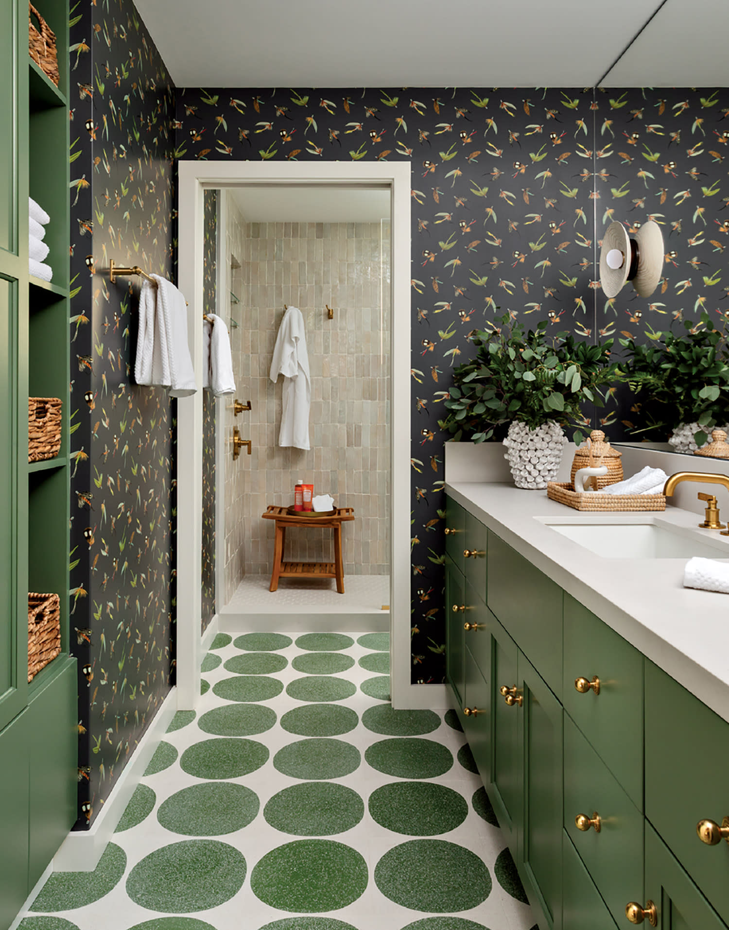 Elegant bathroom with green cabinets, polka dot floor, and floral walls. Features a large plant, woven baskets, and a bright, inviting shower area.