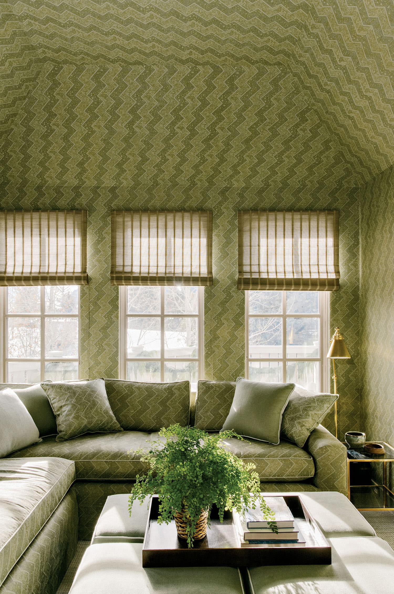 A living room with a wraparound couch, coffee table and green wallpaper on the walls and ceiling. 