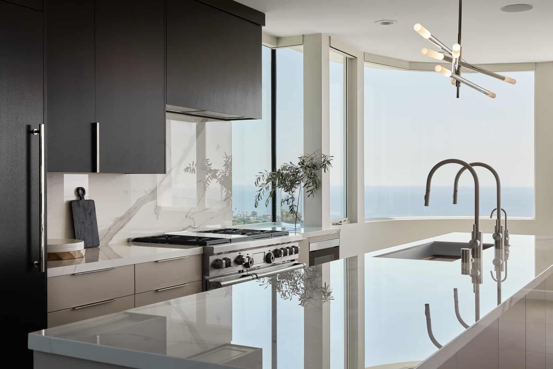 A sleek modern kitchen in Southern California by Payton Addison Interior Design featuring large windows with a stunning view of the ocean. 
