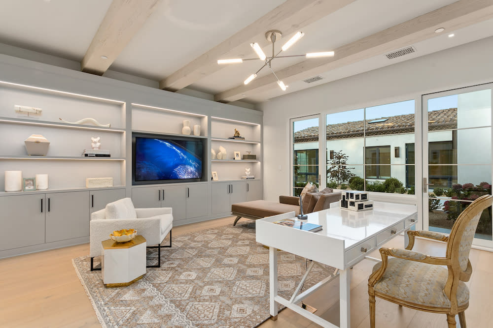 A modern home office with a large TV, white desk and neutral colored sitting area.