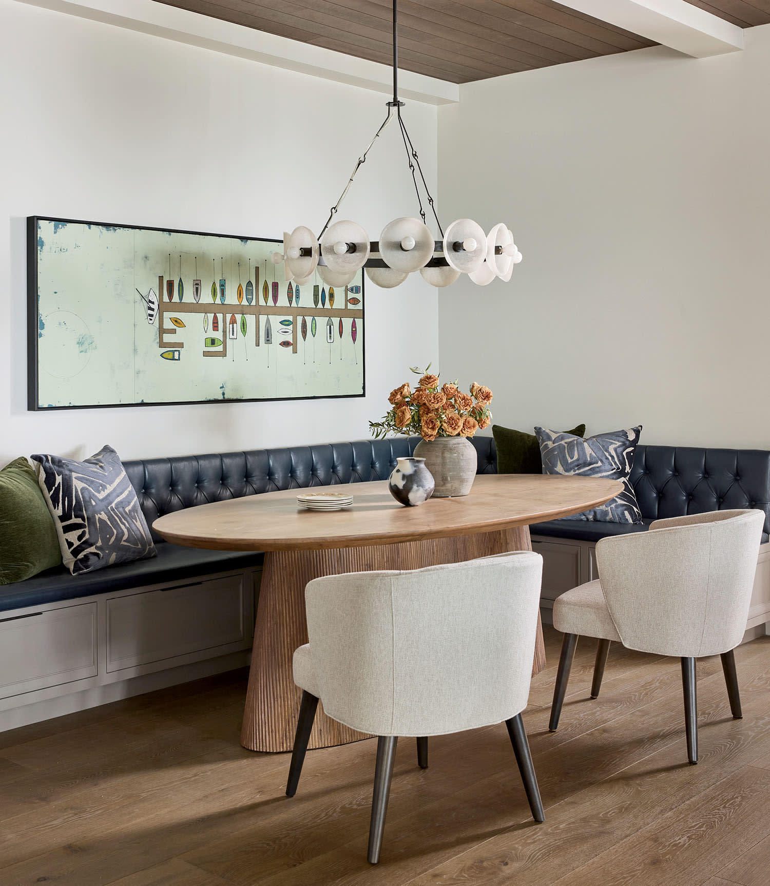 Elegant dining area with an oval wooden table, white chairs, and a dark blue cushioned bench.