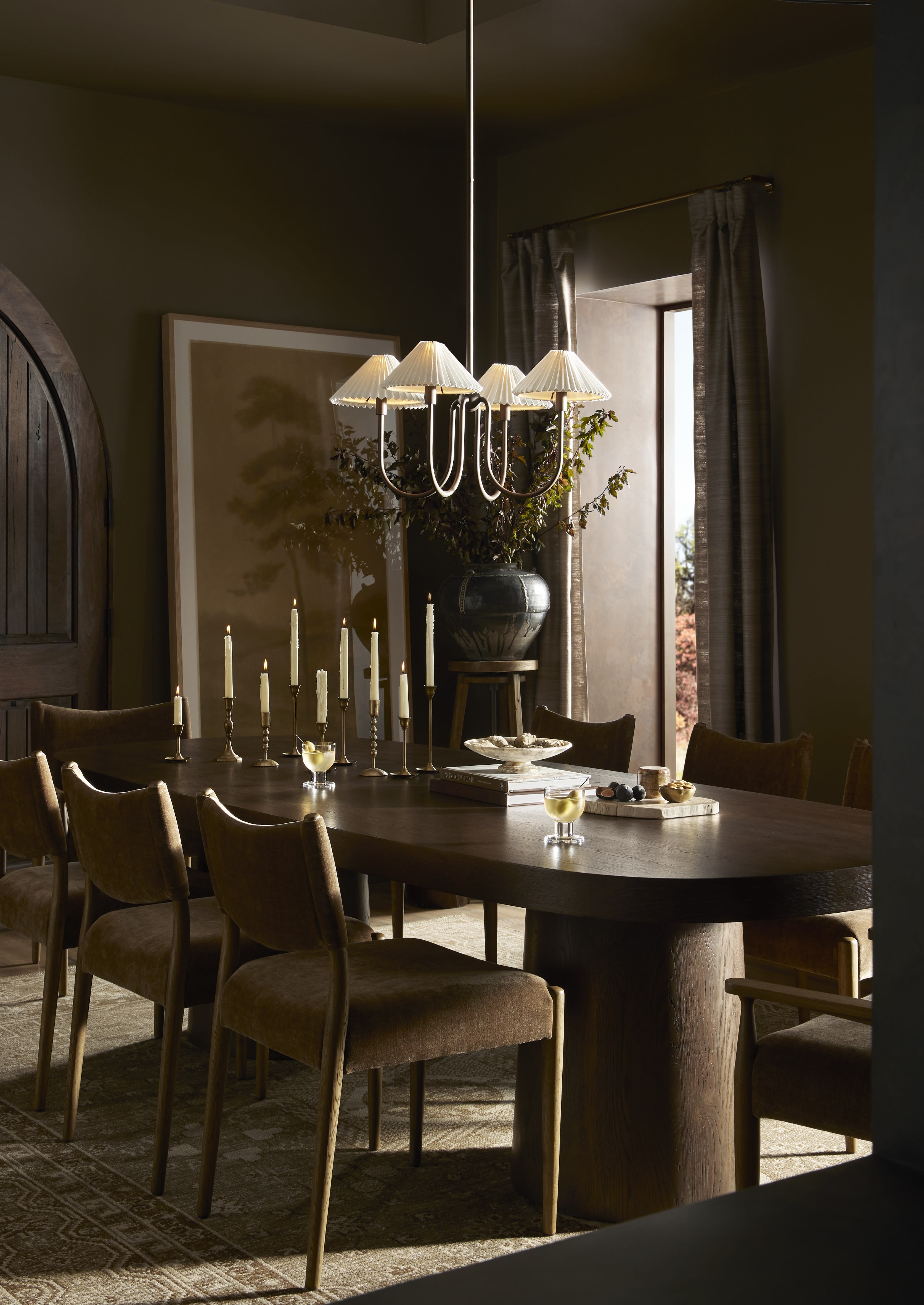 Moody dining room with large, oval wood table and pleated chandelier.