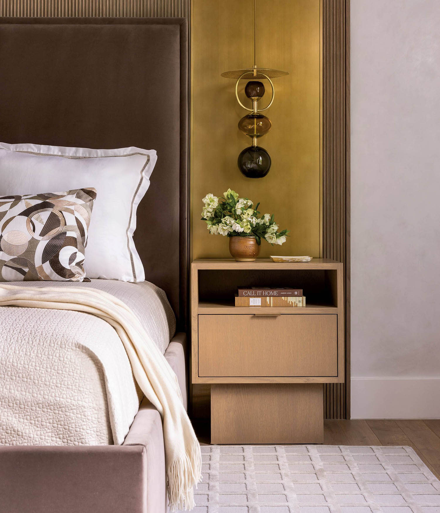 A bed with a brass-inset headboard and wood nightstand with shelf sit on top of a white rug.