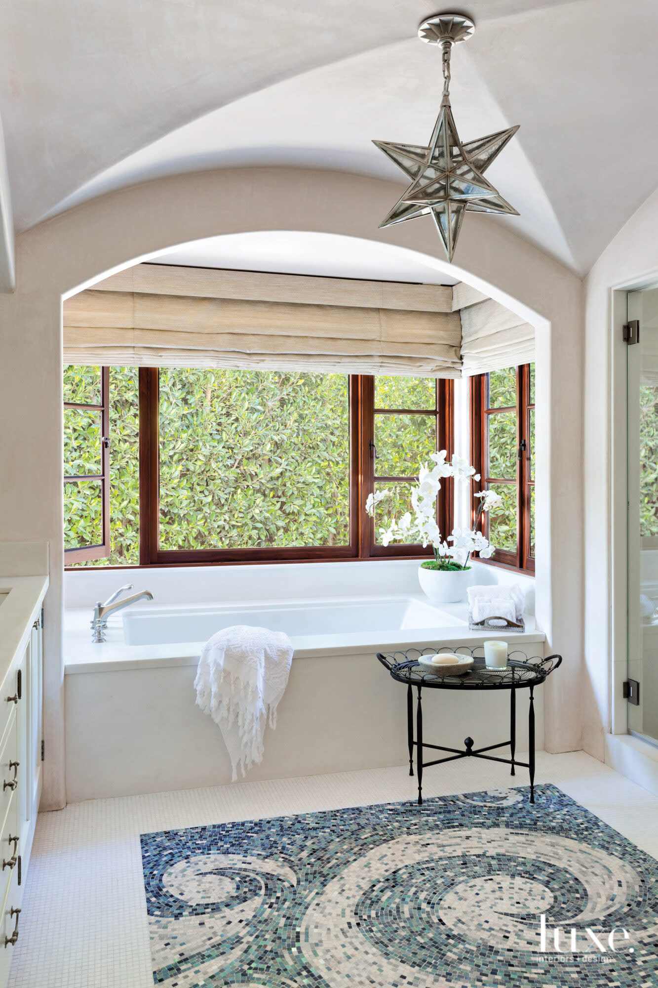 Shot of bathroom with tub below large window and tile mosaic on floor