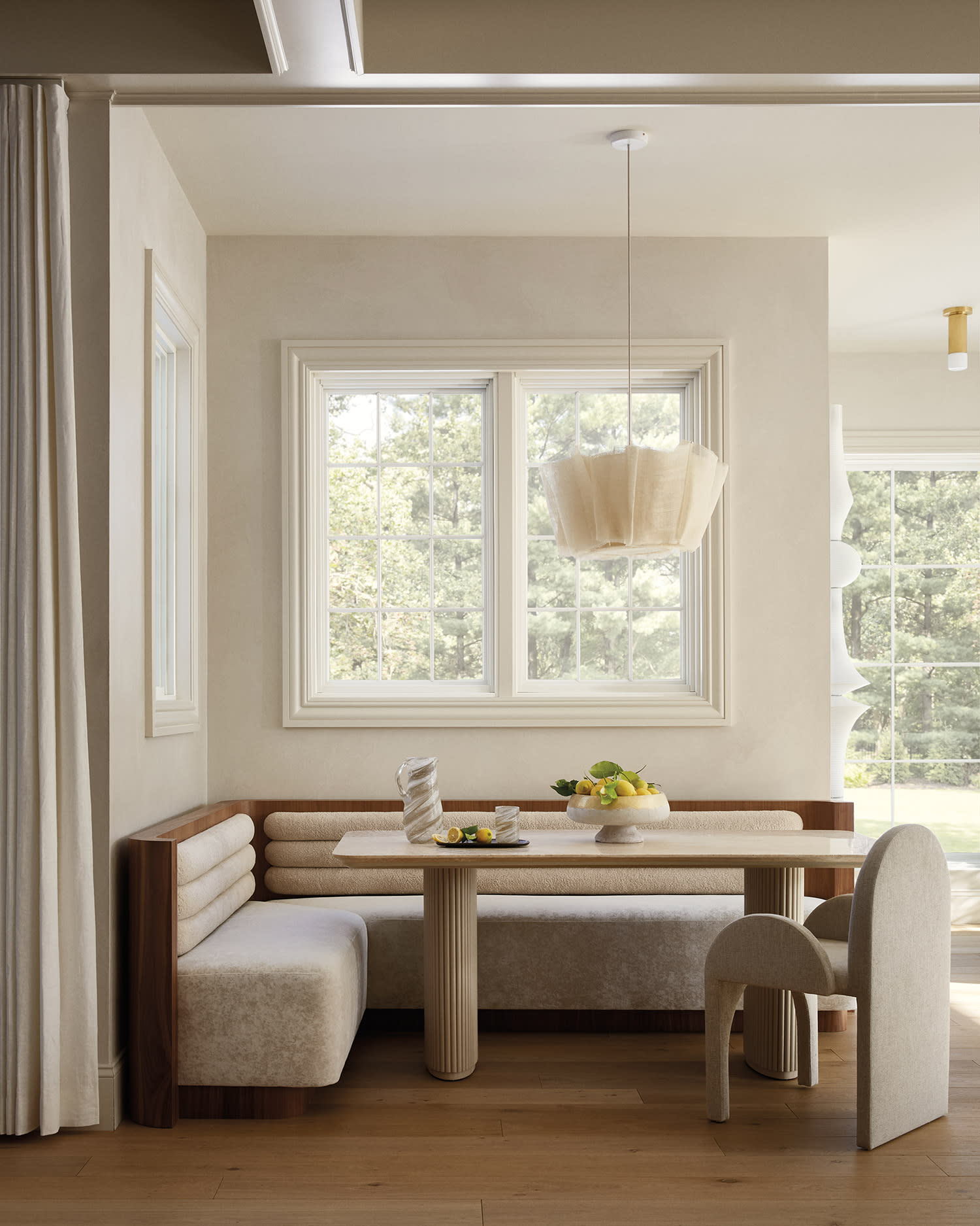 Dining nook with built-in upholstered banquette, light linen chair, wood table, and pendant light.