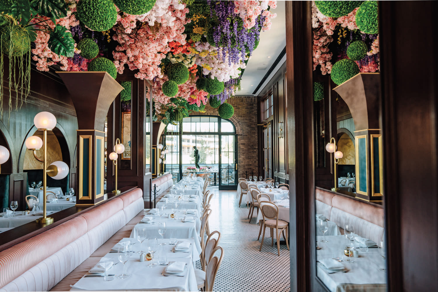 Dining area lined with blush-velvet banquettes below a ceiling installation of pink, purple and green seasonal florals.