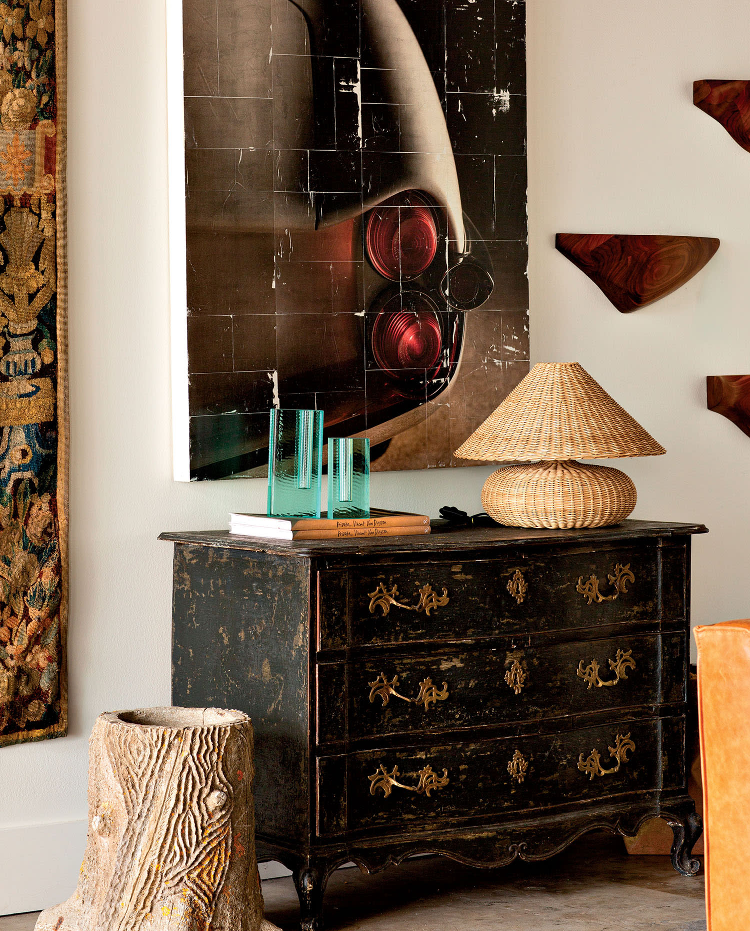 A wood chest of drawers holding a lamp, book and small sculpture, placed underneath artwork.