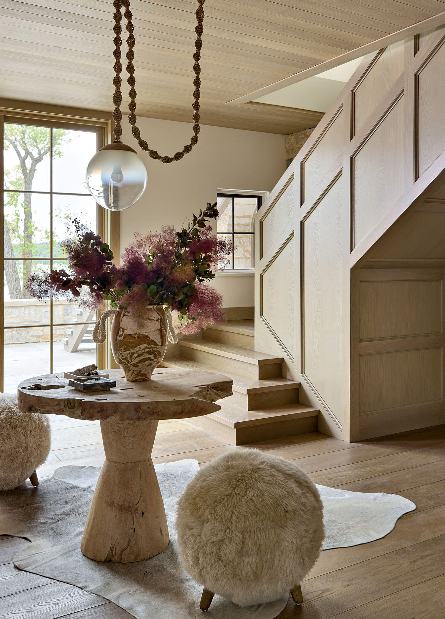 A living area with limewash walls, a table with two circular seats and a chandelier hanging overhead.