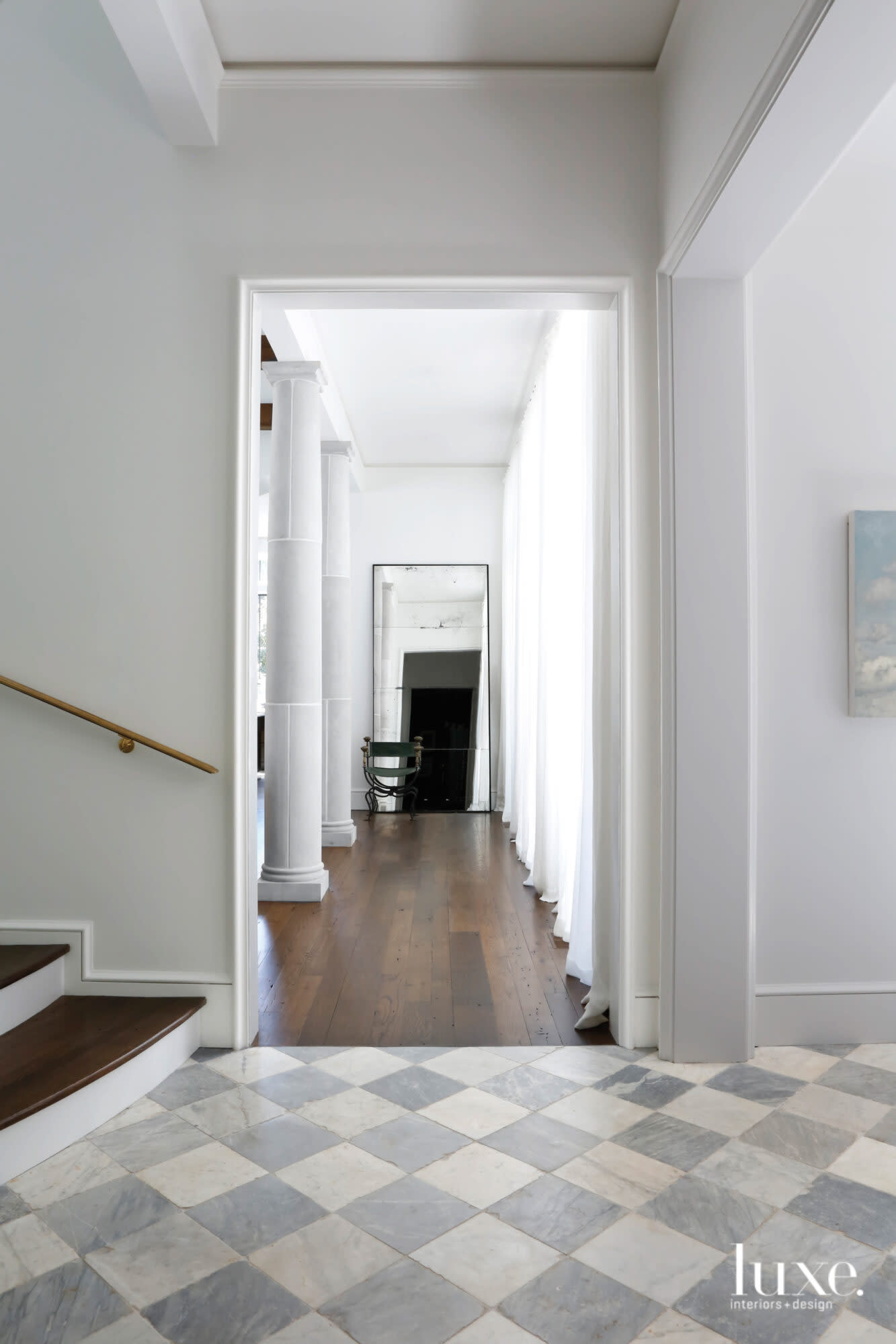 Stair hall leading to long hallway with columns on the left, drapery panels on the right and a leaning tall mirror at center