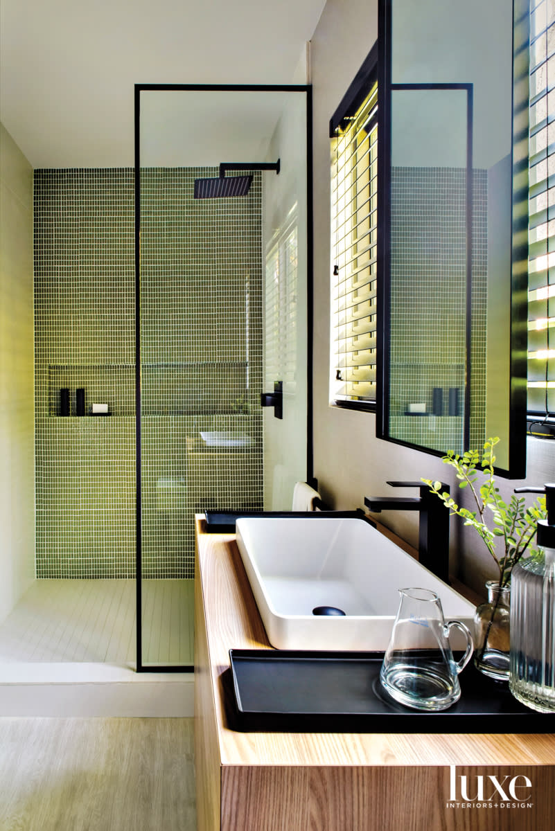 bathroom with green tile shower, black iron frames and white sink on wood vanity