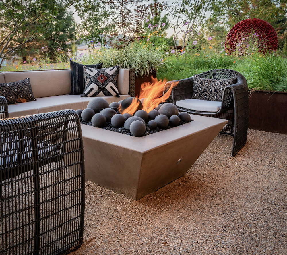 A cozy fire pit in a serene backyard, surrounded by lush greenery and comfortable seating.