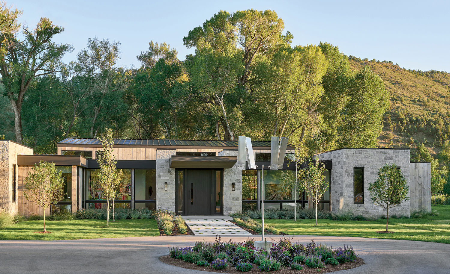 a Ken Bortolazzo sculpture in front of a home with an exterior palette of limestone and barnwood