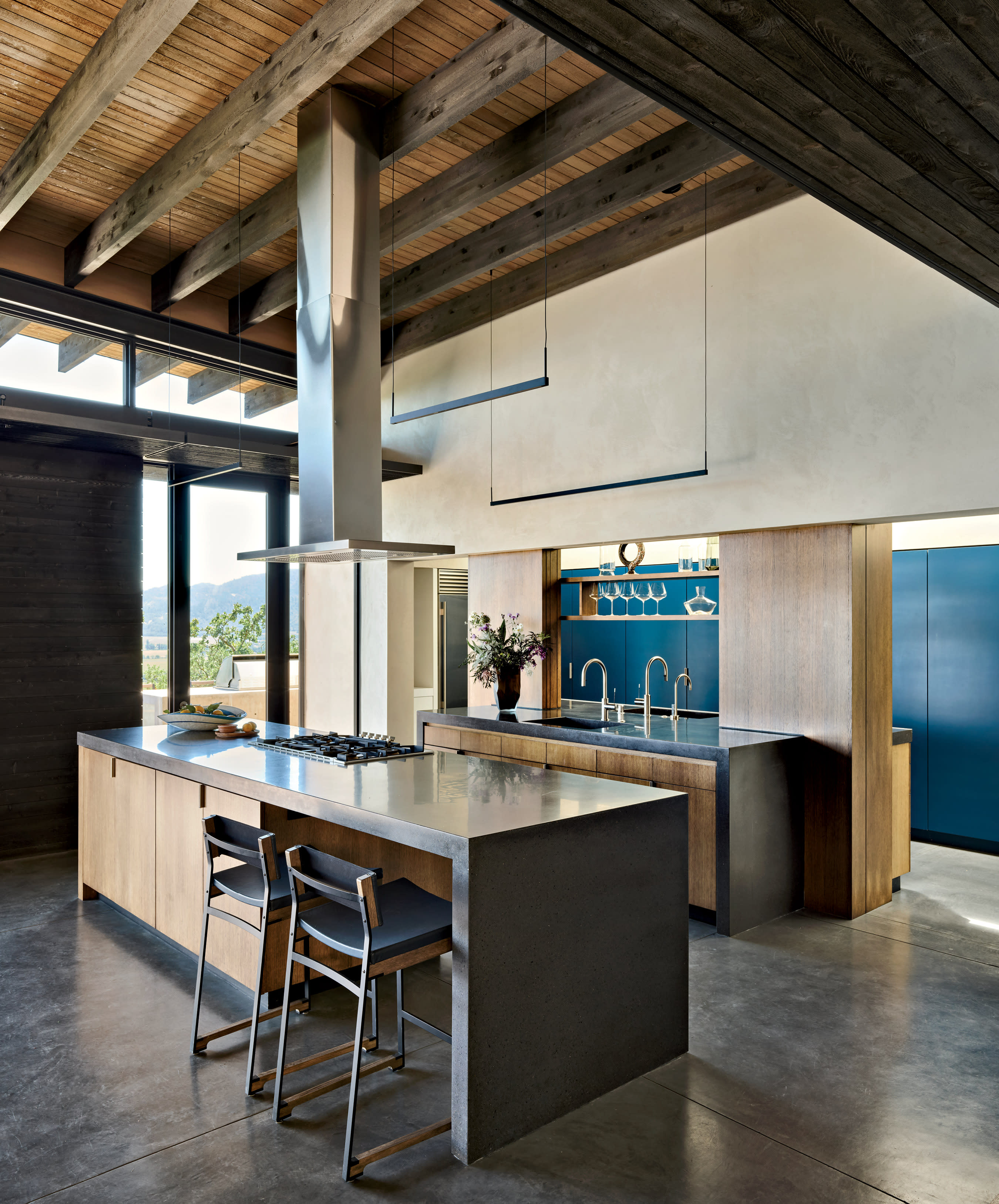 A kitchen with a blue accent wall, concrete countertops, and an island with high-top stools.