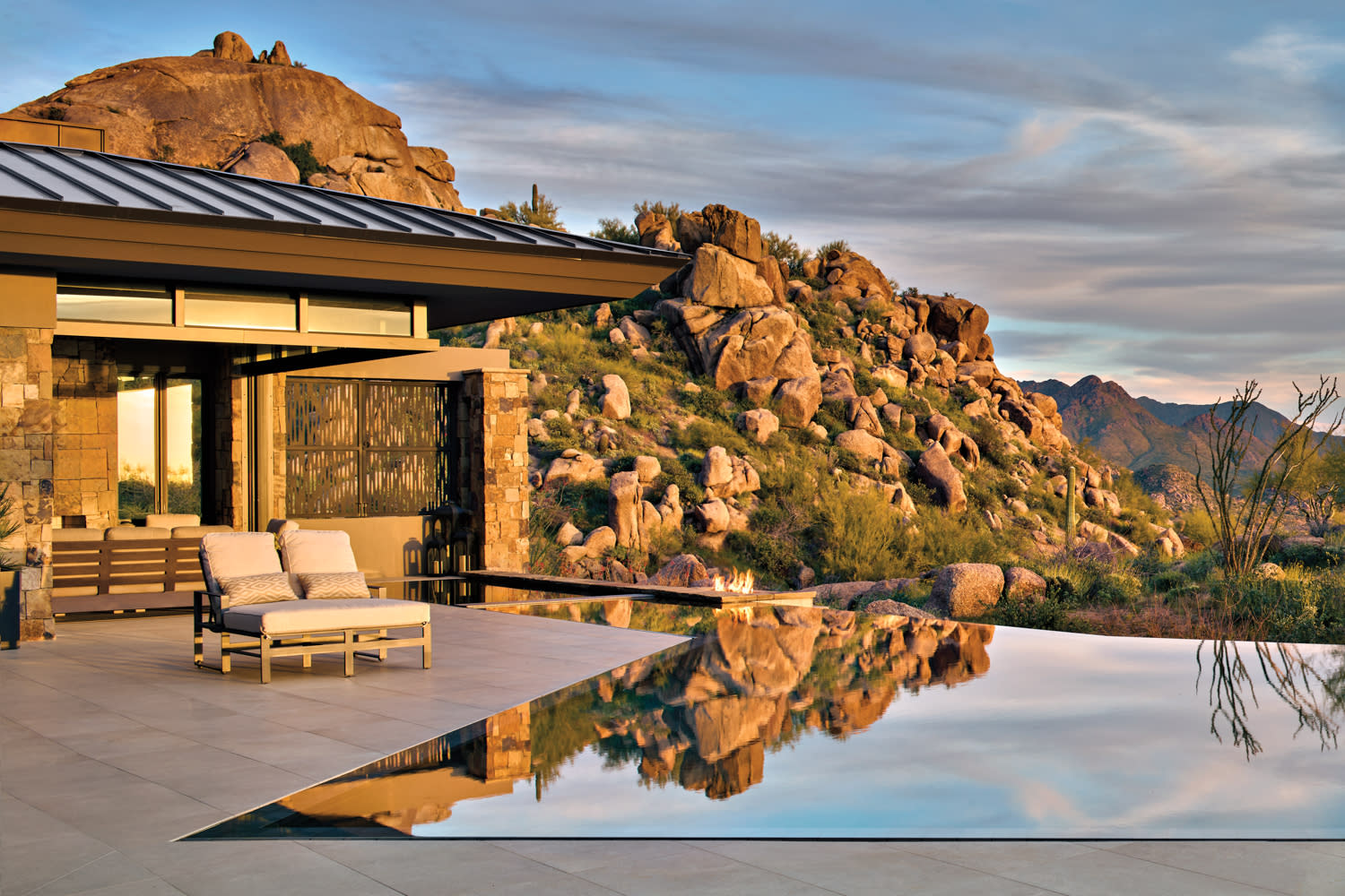 A pair of chaise lounges sit next to an infinity pool on a patio with picturesque mountain views