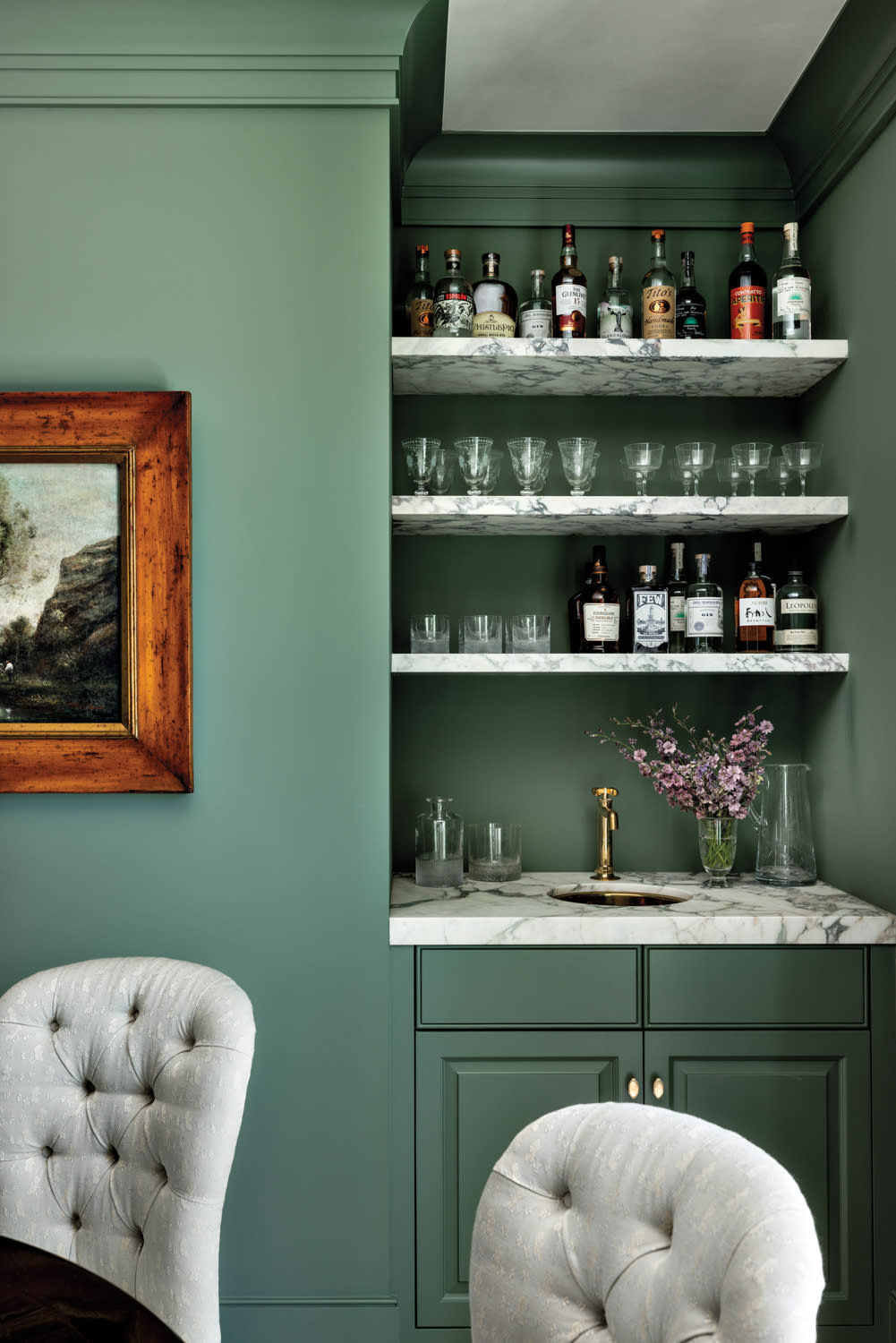 built in wet bar of dining room area, with open marble shelving against green painted walls and glassware on display in home by Marie Carson