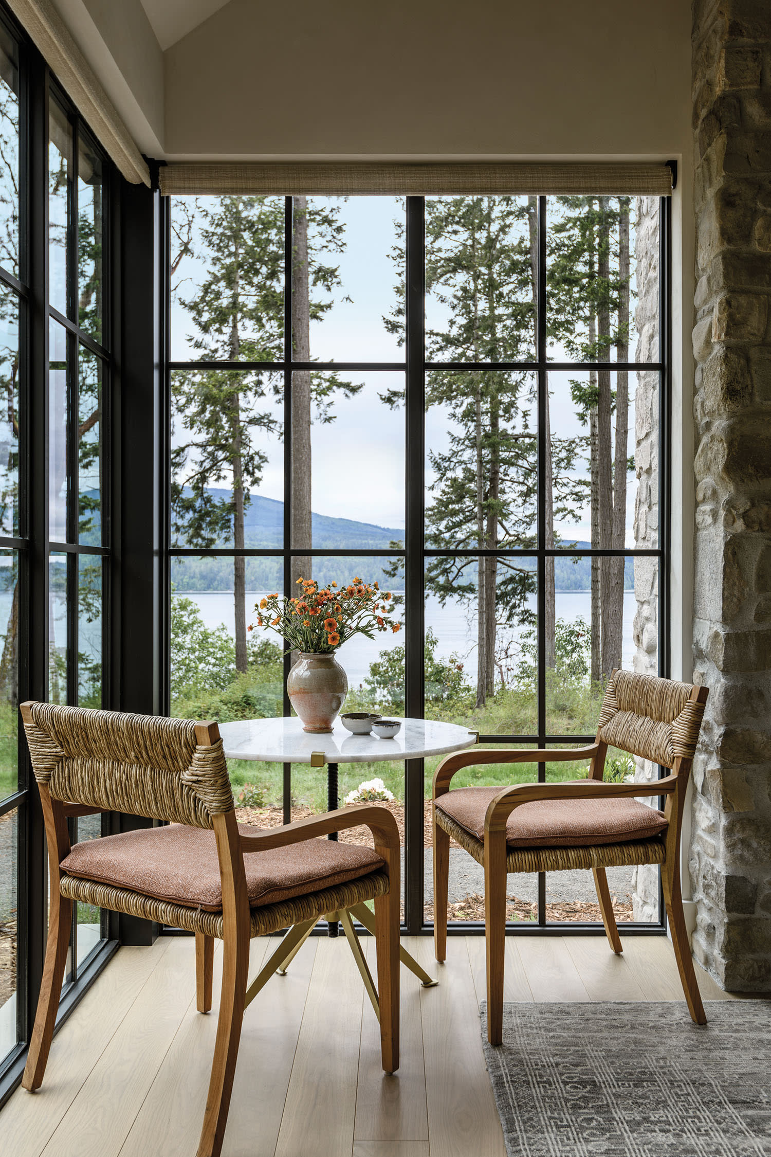 dining corner with floor-to-ceiling windows and woven chairs around a round white table