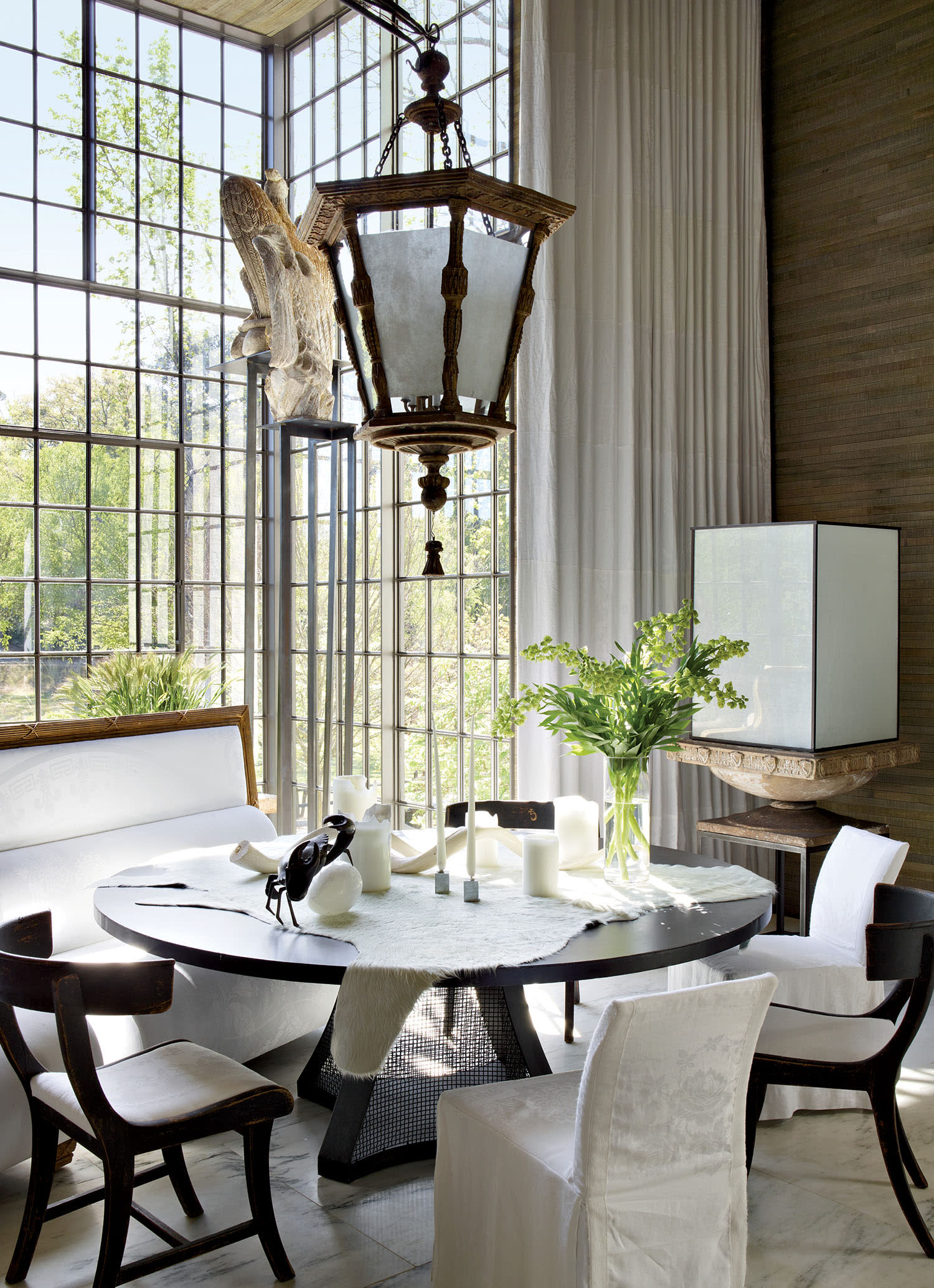 A dining area with a table and chairs, chandelier hanging overhead and floor-to-ceiling windows.